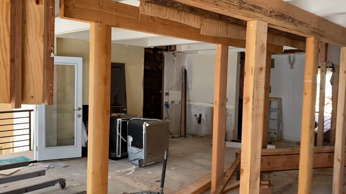 Interior of a house mid-demolition: a row of temporary wood posts carries a beam across the ceiling where a bearing wall has been opened up, with the room beyond stripped to bare studs. Structural demolition from Vince's California contracting years, 2022.